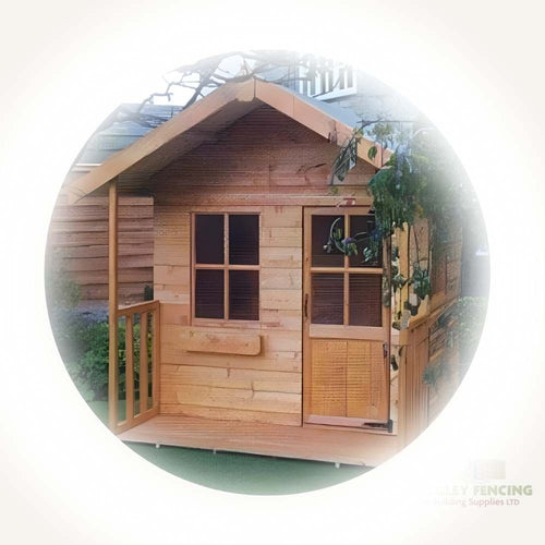 The Hideout Kids Playhouse by Bingley Fencing is a cozy, child-friendly structure featuring a natural wood finish. It boasts a sloped roof, front porch, and windows and is treated with preservatives for safety. This charming wooden playhouse is nestled in a garden area amid lush greenery, offering endless outdoor fun.