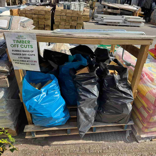 Multiple large Mixed Timber Offcuts Bags by Bingley Fencing, predominantly black with one blue, are arranged on a wooden pallet outdoors. Ideal for DIY projects, these surplus timber bags feature a sign reading "Timber Off Cuts" that provides information on their availability and pricing.