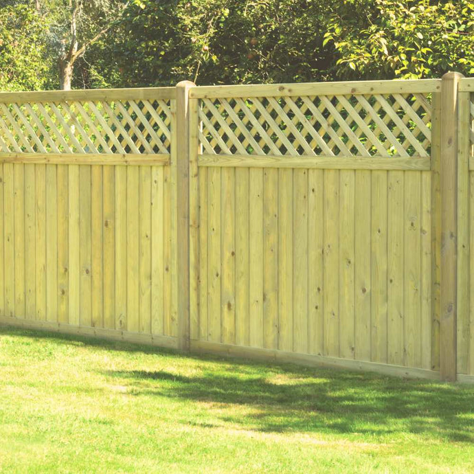 A KDM Tongue & Groove Lattice Top Fence Panel stands on a grassy lawn, featuring vertical pressure-treated panels and a decorative lattice top, surrounded by trees and greenery.