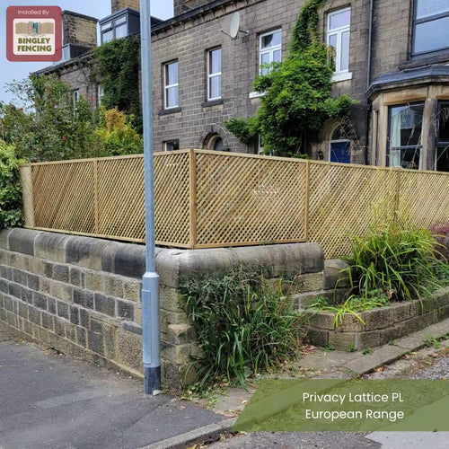 A beige privacy lattice fence is installed on top of a stone wall outside a residential building with stone walls and green plants. Text reads: Install by Bingley Fencing and Privacy Lattice PL European Range.