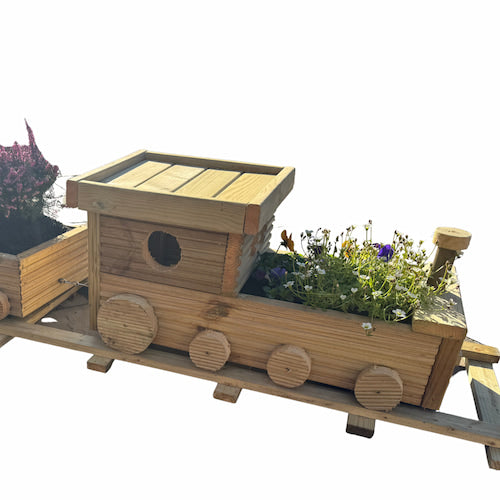 A wooden planter shaped like a train engine, with flowers growing in the compartments. The train sits on a wooden track and has round wheels and a small window on the engine.