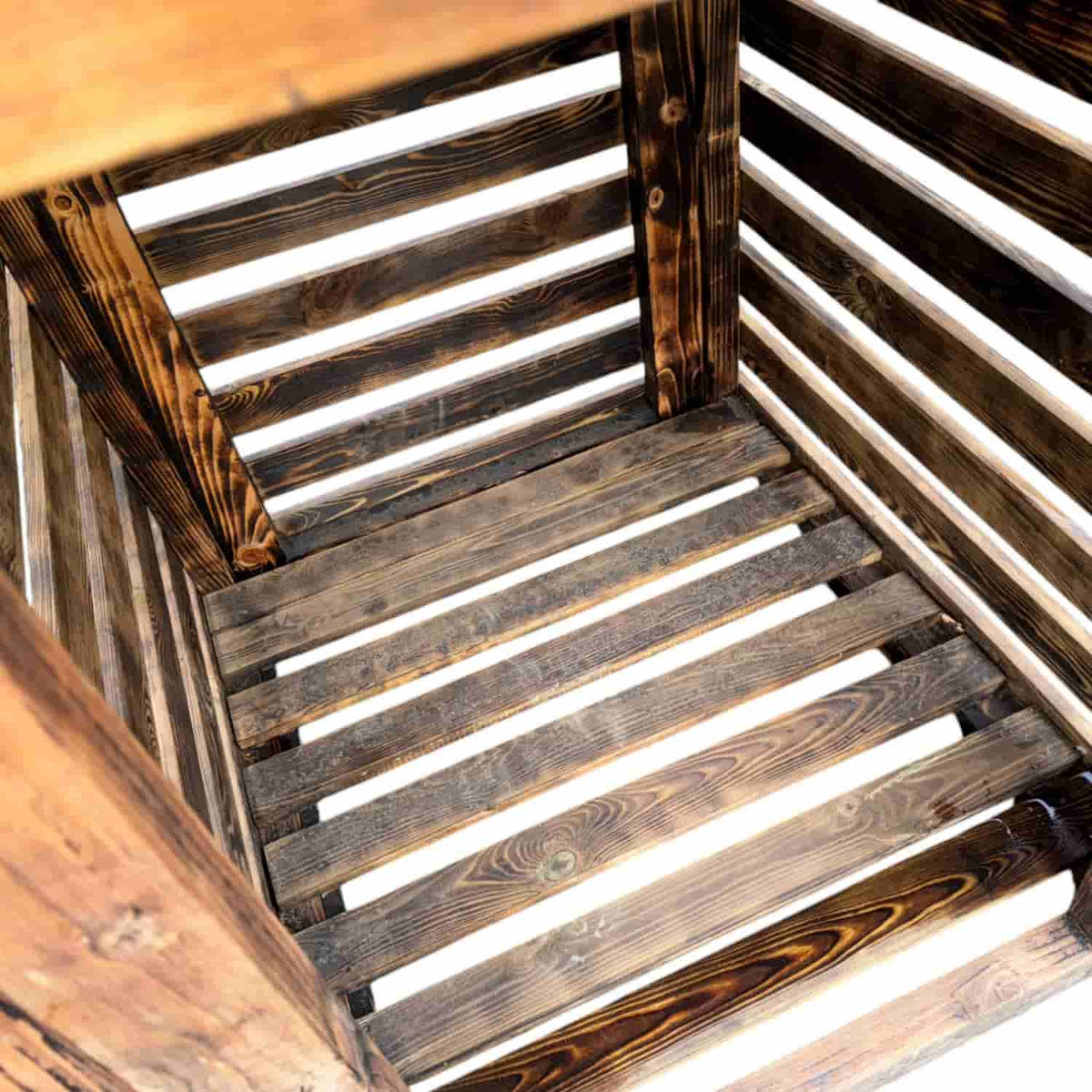 The empty interior of Bingley Fencings Unique Log Store features darkly stained, rugged wooden slats with a rustic charm. Light filtering through highlights the timber grain and spaces between the slats, creating a captivating effect. All sizes available.