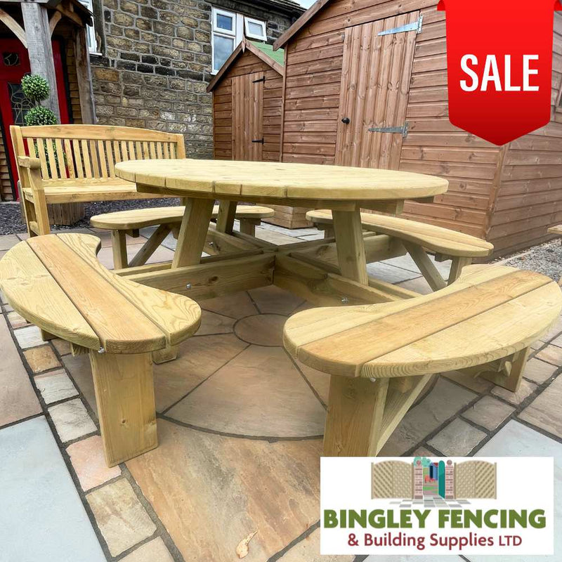 Load image into Gallery viewer, Elite Round Table &amp; Bench Seat **Reduced**, crafted by KDM from tanalised timber, is attractively placed on a stone patio. The set features attached benches, with a wooden bench and shed visible in the background. A red SALE tag is prominently displayed in the top right corner, while Bingley Fencing &amp; Building Supplies LTD's logo can be seen at the bottom.
