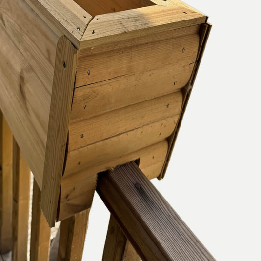 Close-up of the Bingley Fencing Fence Top Planter – Wooden Decking & Balustrade Planter mounted on a balcony railing, highlighting the side and a portion of the bottom support structure. Perfect for use as decking or fence planters, this design integrates effortlessly into outdoor spaces. The background is plain and light-colored.