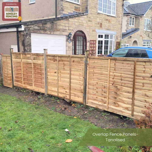 A row of Bingley Fencing Overlap Fence Panels- Tanalised installed along a grassy yard in front of a house with stone walls and a blue car parked in the driveway.