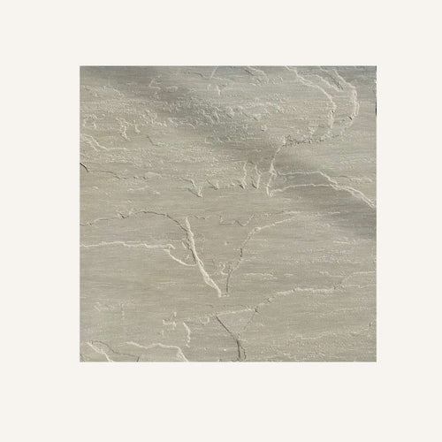A square sample of Bingley Fencing's Raj Green Indian Sandstone Paving Slabs, featuring a light beige textured finish with irregular, slightly raised lines and patterns resembling natural stone on an off-white background.
