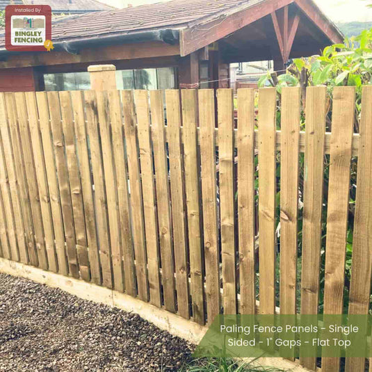 A single-sided paling fence with 1 gaps and a flat top by Bingley Fencing lines a gravel path in front of a wooden house. Text: Paling Fence Panels - Single Sided - 1 Gaps - Flat Top by Bingley Fencing.