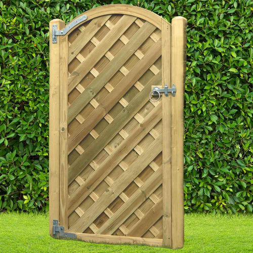 The KDM V’ – Arched Euro-Gate - VAG180, featuring a lattice design and metal hinges, stands closed against a lush green hedge and grass, showcasing the elegance of heavy-duty timber construction.