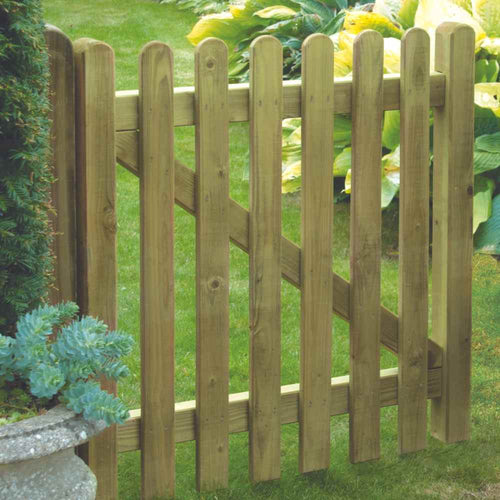 The Premium Round Top Picket Gate – PPG90 by KDM, surrounded by lush greenery, features vertical slats with rounded tops and diagonal support bars, adding rustic charm to the landscape.