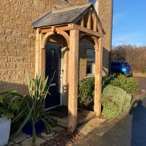 Load image into Gallery viewer, Front door porch or canopy in european solid oak with curved rafters and vertical legs and slate roof.
